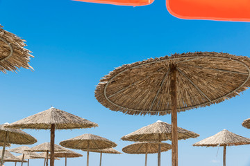 Wicker and textile orange umbrellas on the beach. Blue sky.