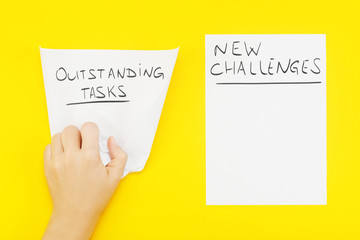 Hand wrinkles a piece of paper with phrase: outstanding tasks, and nearby blank sheet of paper with phrase: New challenges. The concept of setting new goals, and recognition of outstanding tasks.
