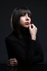 Young beautiful girl in a business style in black clothes with haircut at the desktop. Studio shot.