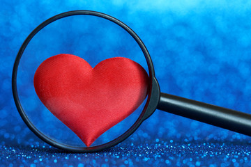 Classic red silk heart under a magnifying glass on a blue background. Choosing a loved one. Happy...