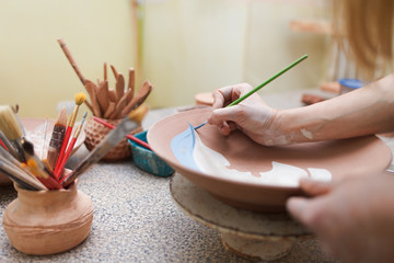 Potter woman paints a ceramic plate. Girl draws with a brush on earthenware. Process of creating...