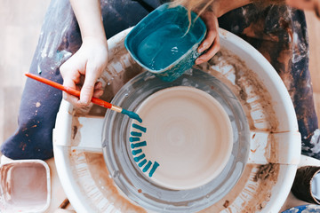 Professional potter works on painting plates in the workshop. Woman paints a ceramic plate with a brush and blue paint