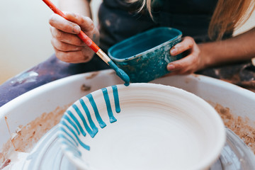 Professional potter works on painting plates in the workshop. Woman paints a ceramic plate with a...