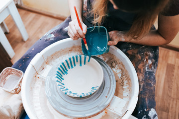 Professional potter works on painting plates in the workshop. Woman paints a ceramic plate with a...