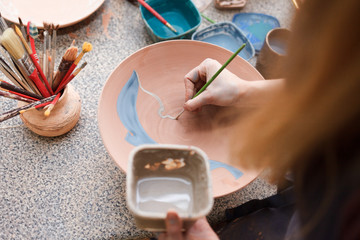 Potter woman paints a ceramic plate. Girl draws with a brush on earthenware. Process of creating...