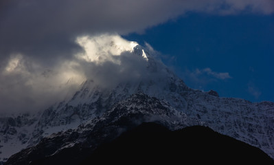 Fototapeta na wymiar A view of the summit of the Himalayan peak of Annapurna South lit by the sun as clouds hover around it as seen from the Annapurna Base Camp trail.