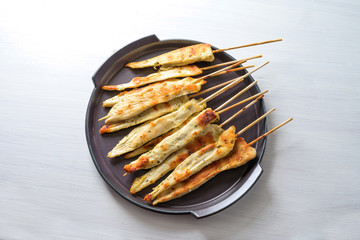 Roasted Mediterranean chicken skewers, finger food snack for a festive New Year party on a dark purple plate, white painted wooden table with copy space, high angle top view from above