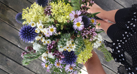 Bouquet from the garden during Summer (Hydrangea, Oregano). Hand holding the flowers. In the background leg and skirt, Standing on an old wooden floor.