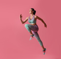 Athletic young woman running on pink background, side view