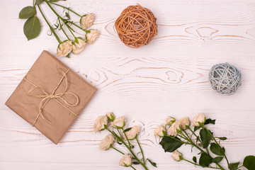 Gift box wrapped in kraft paper, rattan balls and flower on a white wooden background from above. Flat lay.