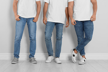 Group of young men in stylish jeans near light wall, closeup
