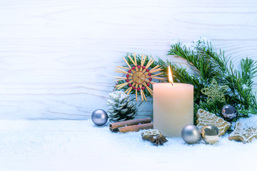 Burning candle and Christmas decoration on snow against a white wooden background, copy space