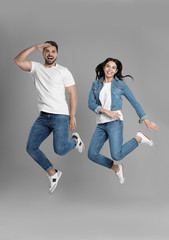 Fototapeta na wymiar Young couple in stylish jeans jumping on grey background