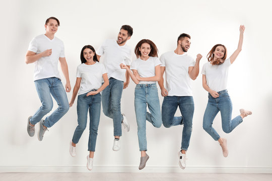 Group of young people in stylish jeans jumping near white wall