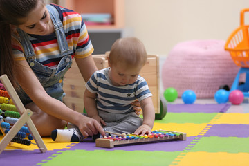 Teen nanny and cute little baby playing with xylophone at home - obrazy, fototapety, plakaty