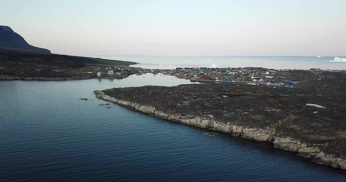 4K Aerial Drone flight in Disko Bay Greenland. Arctic city of Qeqertarsuaq in Disko Island. Colourful houses during sunset and midnight sun. Icebergs in Background.