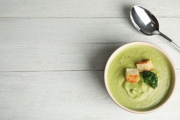 Delicious broccoli cream soup with croutons served on white wooden table, flat lay. Space for text