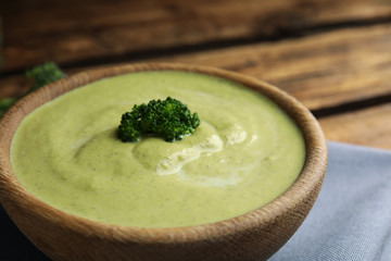 Wooden bowl of delicious broccoli cream soup on table, closeup