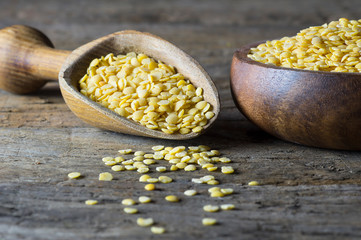 Uncooked raw yellow lentil in wooden shovel and bowl on wooden rustic table, heap of legume lentil background (Lens culinaris)
