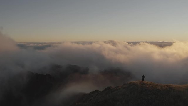 Aerial shot over a hiker at the summit of a mountain during sunset. Drone view in 4k. 