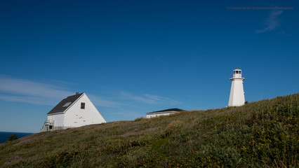 A white lighthouse high on a hill with a couple of white outcrop buildings. The sky is bright blue...