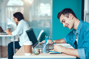 Happy young man is writing in notebook