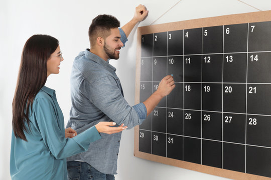 Colleagues writing with chalk on board calendar