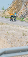 A couple of two bikers male and female are riding their bikes uphill on a sunny day wearing sports gear.