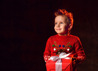 Little happy boy in a red sweater with an image of a rudolph deer holding a present from santa