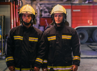 Fototapeta premium Portrait of two young firemen in uniform standing inside the fire station .