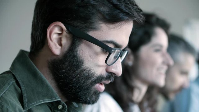 Side view of focused man in eyeglasses working. Young people sitting in row and typing on laptops. Working concept