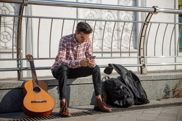 Fototapeta na wymiar Young guitarist sitting and using phone in the street