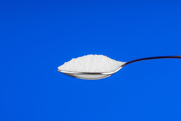 Spoon with white sugar on a blue background