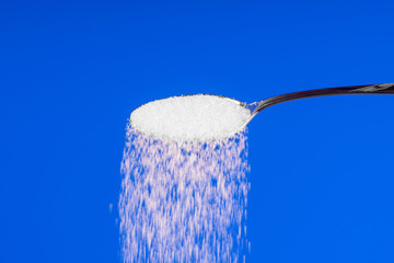 Fototapeta na wymiar Falling sugar from a spoon on a blue background