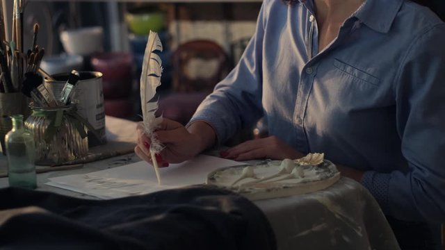 Artist female is working with bird's feather and ink