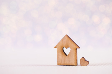 Wooden icon of house with hole in form of heart on light glitter shiny background with bokeh lights.