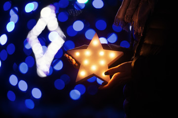 Female hands holding glowing white LED star with blue festive Christmas illumination on background.