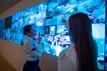 Security guards standing in front of a large CCTV monitor at the main control room while reading...