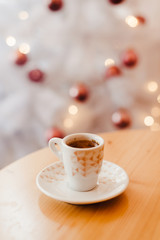 Cup of espresso or short coffee in white cup in cosy Christmas arrangement, festive decoration with white bokeh background, copy space