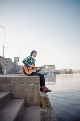 Happy guy with headphones playing guitar outdoors