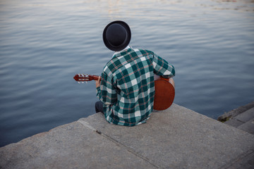 Young male is sitting with guitar outdoors