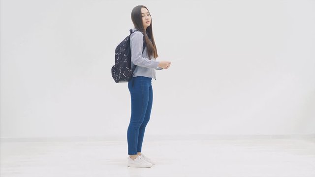 Beautiful asian young teenager girl, with backpack behind shoulders, appearing on the white background with a map in her hands, poking her head around, and disappearing.