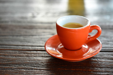 Close up Orange coffee cup on black wood table near window at cafe.