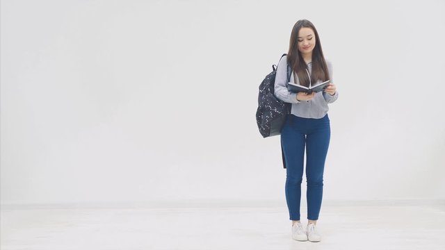 An asian schoolgirl appearing on a white background with a backpack, opening black book, looking at it, closing, posing.