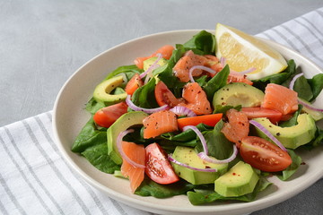 Mediterranean Avocado Salmon Salad with spinach, cherry tomatoes, avocado and red onion dressing. Concept for a tasty and healthy meal. Vegan food