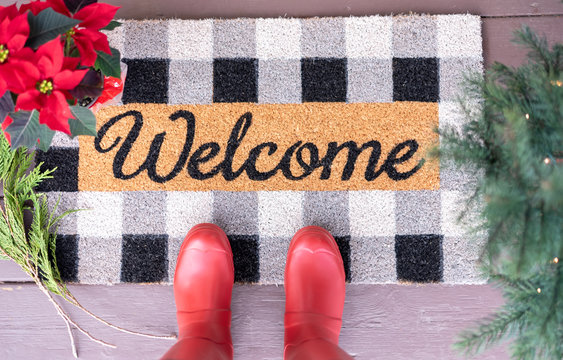 Welcome mat on the front porch with red boots and holiday greens