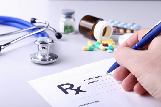 Close-up of doctor's hands writing prescription and holding bottle with pills. Healthcare, medical and pharmacy concept.