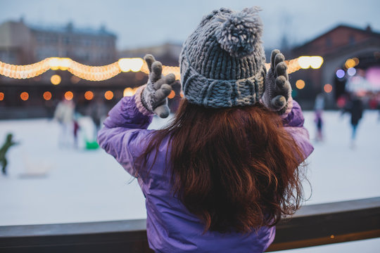 Girl watching on the ice rink with happy people ice skating in the background, concept of ice skating in winter, holiday christmas time, with new year decoration and illumination, Helsinki, Finland