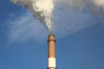 Factory chimney smoking with dense white smoke on blue sky background. Industrial pollution of air,...