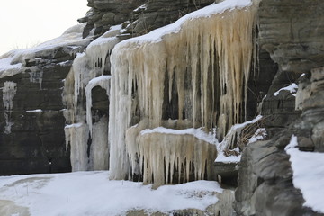 Fototapeta na wymiar Frozen waterfall in gray rocks. Icicles and snow in winter cold temperature.